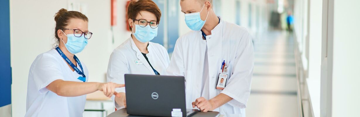Kuvassa kaksi lääkäriä ja hoitaja tarkastelevat tietoja kannettavalta tietokoneelta.