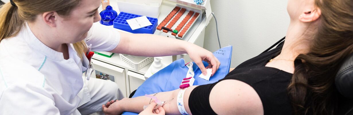 Kuvassa hoitaja ottaa asiakkaalta verinäytteen laboratoriossa.
