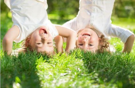 Kaksi lasta seisoo päällään nurmikolla, isosti hymyillen.