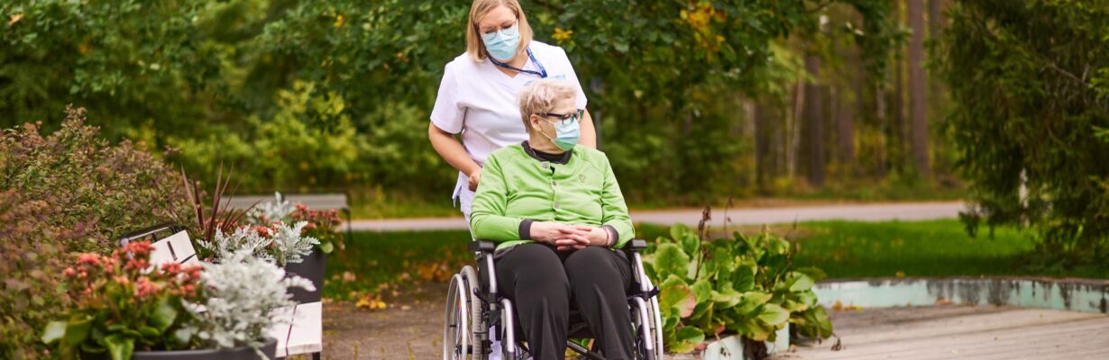 Kuvassa hoitaja ulkoilee pyörätuolipotilaan kanssa.
