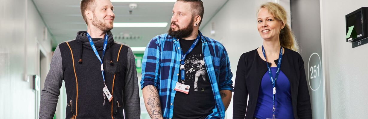 Sosiaalipalveluiden työntekijöitä kävelemässä toimitilan käytävällä hymyillen.