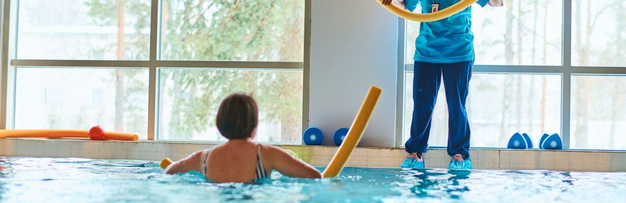 Kuvassa naishenkilö kuntoilee uima-altaassa fysioterapeutin ohjeistuksella.