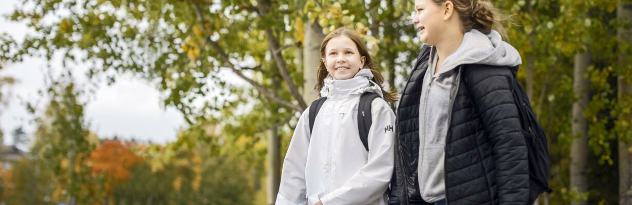 Kaksi koululaista kävelee hymyillen koulun pihalla.