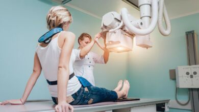 Kuvassa otetaan röntgenkuvat nuoren naisen jaloista. Työntekijä säätää laitetta.