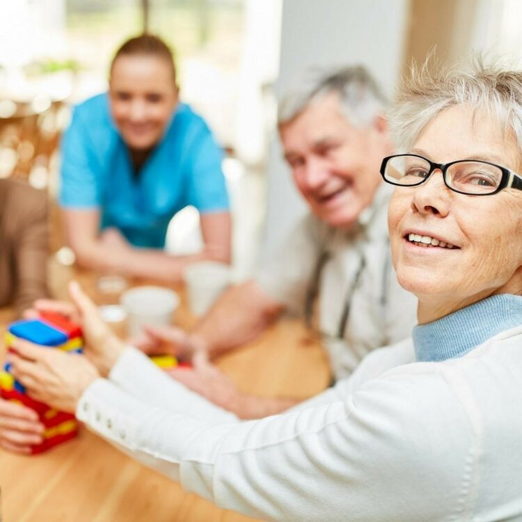 Kuvituskuvassa ikäihmisiä kahvipöydän äärellä pelaamassa muistipeliä yhdessä hoitajan kanssa.