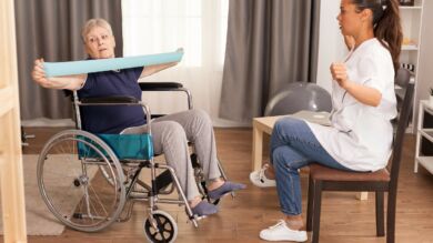 Fysioterapeutti kuntouttaa pyörätuolissa istuvaa ikääntynyttä asiakasta.