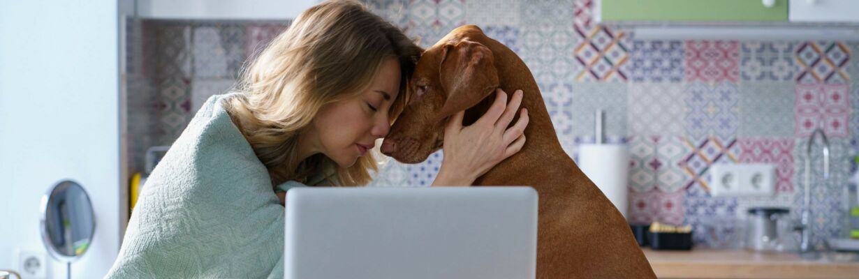Kuvassa masentunut nainen sekä koira tietokoneen äärellä.