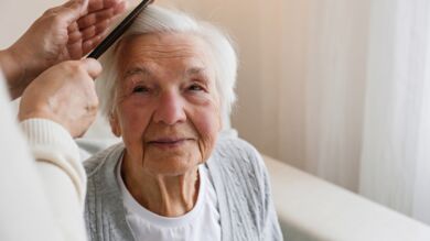 Kuvan henkilö kampaa ikääntyneen naisen hiuksia.