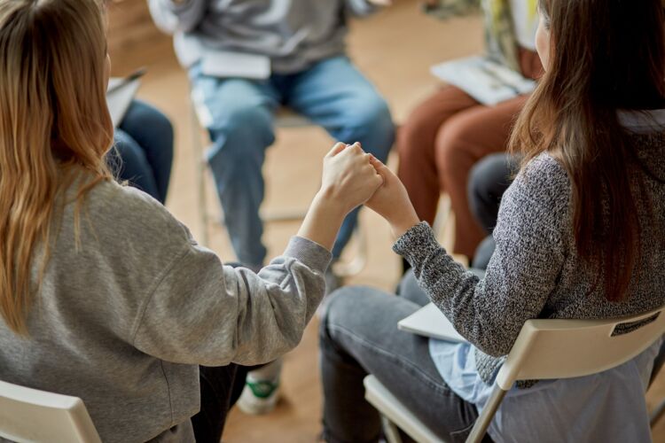 Kuvassa nuoria aikuisia ringissä ryhmäterapiassa. Nuoret pitävät toisiaan kädestä kiinni.