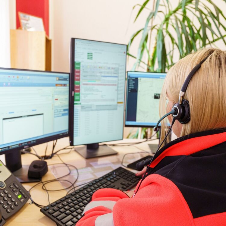 Kuvassa keskitetyn puhelinpalvelun työntekijä tietokoneen äärellä, headset -kuulokkeet korvillaan.