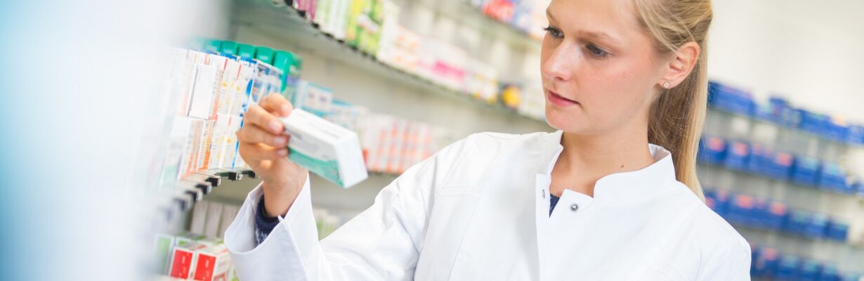 Kuvassa farmaseutti tarkastelee lääkepakettia apteekinhyllyn luona.
