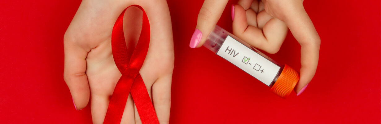 Kuvassa kädet, joista toisessa AIDSia symboloiva punainen AIDS-nauha, toisessa kädessä HIV-verinäyteputkilo.
