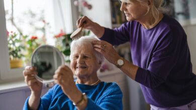 Kuvan henkilö kampaa ikääntyneen naisen hiuksia.