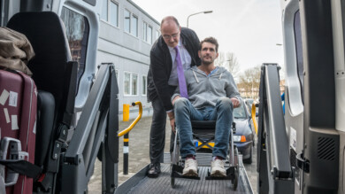 Kuljettaja avustaa pyörätuolissa olevaa miestä tilataksiin.