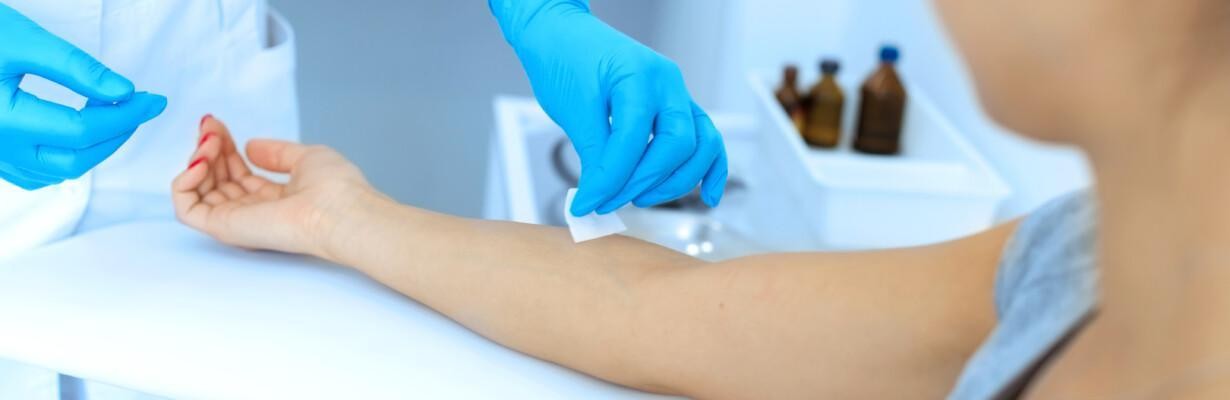 Hoitaja puhdistaa pistoskohtaa naisen käsivarressa verikoetta varten.